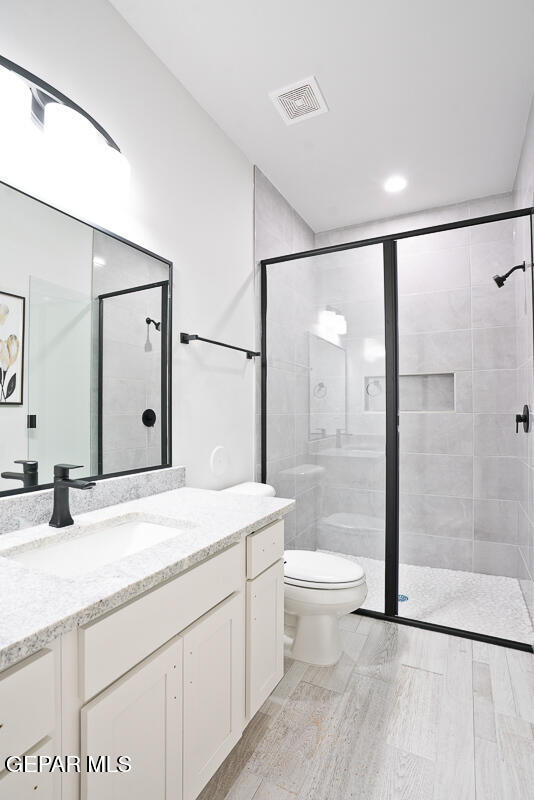 bathroom featuring vanity, a shower with shower door, and toilet