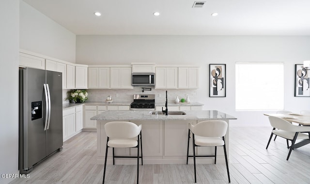 kitchen featuring sink, an island with sink, stainless steel appliances, light stone countertops, and white cabinets