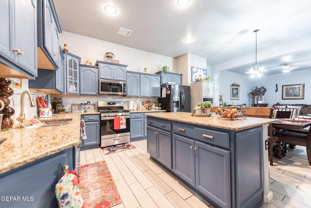 kitchen with light stone countertops, appliances with stainless steel finishes, sink, blue cabinetry, and hanging light fixtures