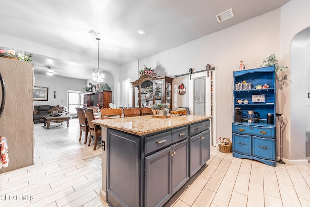 kitchen with light stone countertops, a center island, hanging light fixtures, a barn door, and light wood-type flooring