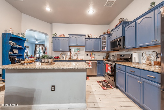 kitchen featuring light stone counters, stainless steel appliances, ceiling fan, sink, and blue cabinetry