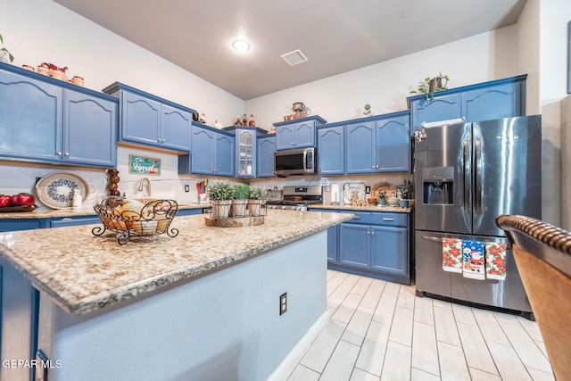 kitchen with blue cabinetry, appliances with stainless steel finishes, light stone counters, and a kitchen island