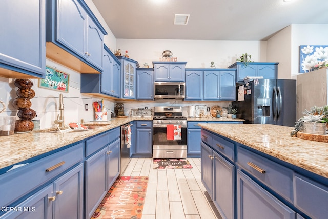 kitchen with blue cabinetry, stainless steel appliances, light stone countertops, and sink