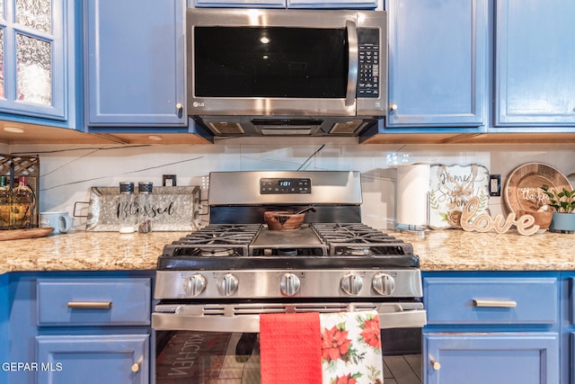 kitchen with light stone counters, blue cabinets, stainless steel appliances, and tasteful backsplash