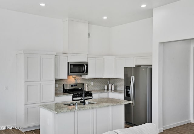 kitchen with a center island with sink, dark hardwood / wood-style floors, appliances with stainless steel finishes, light stone counters, and white cabinetry