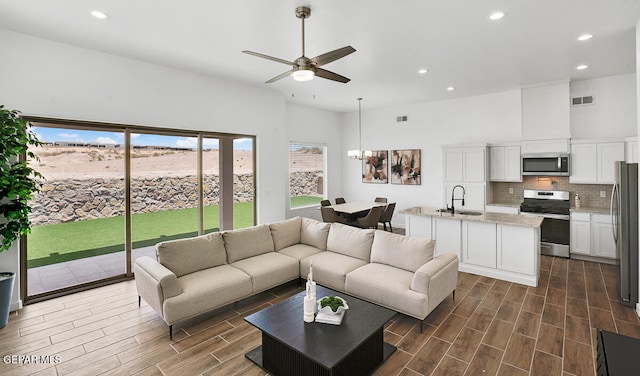 living room with ceiling fan with notable chandelier, sink, a towering ceiling, and dark wood-type flooring