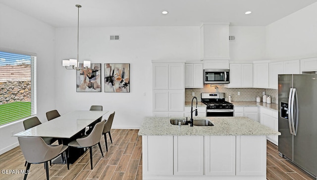 kitchen featuring pendant lighting, light stone countertops, appliances with stainless steel finishes, an island with sink, and white cabinets