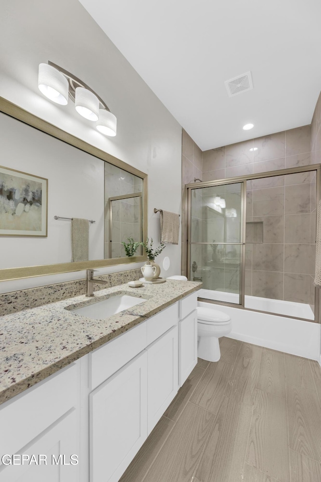 full bathroom featuring wood-type flooring, combined bath / shower with glass door, vanity, and toilet