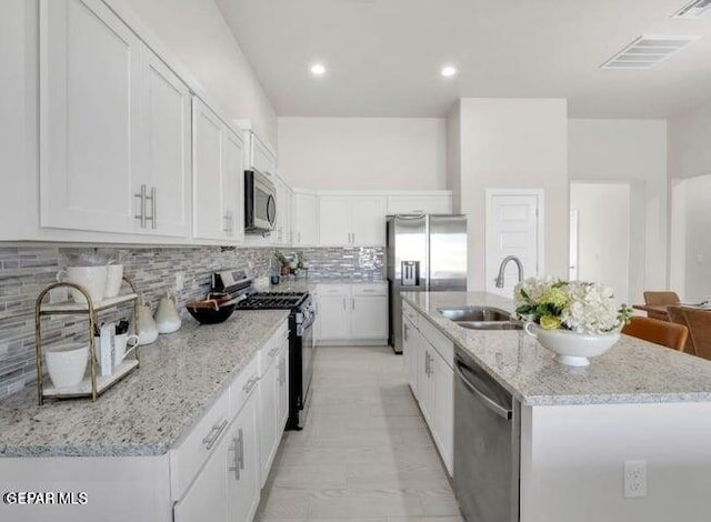 kitchen with light stone counters, a center island with sink, white cabinets, and stainless steel appliances