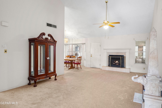 carpeted living room with a tiled fireplace, ceiling fan, and high vaulted ceiling