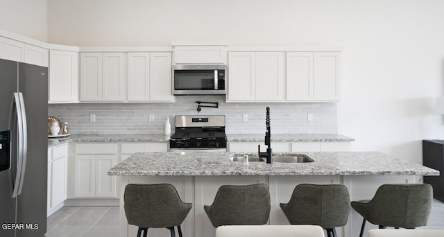 kitchen with sink, stainless steel appliances, light stone countertops, white cabinets, and a center island with sink