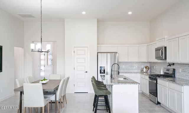 kitchen with appliances with stainless steel finishes, a towering ceiling, pendant lighting, an island with sink, and white cabinets