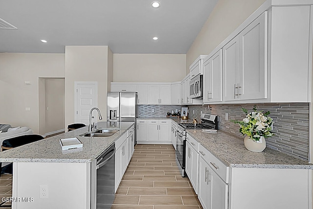 kitchen featuring appliances with stainless steel finishes, sink, white cabinets, light stone counters, and a kitchen island with sink