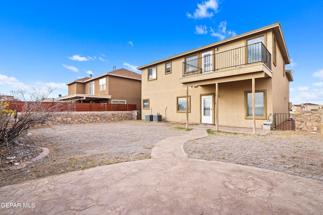 rear view of house featuring central AC unit, a balcony, fence, a patio area, and stucco siding