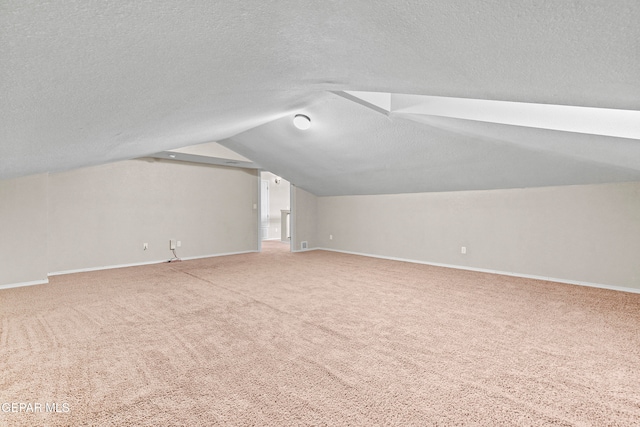 additional living space featuring baseboards, vaulted ceiling, a textured ceiling, and carpet flooring