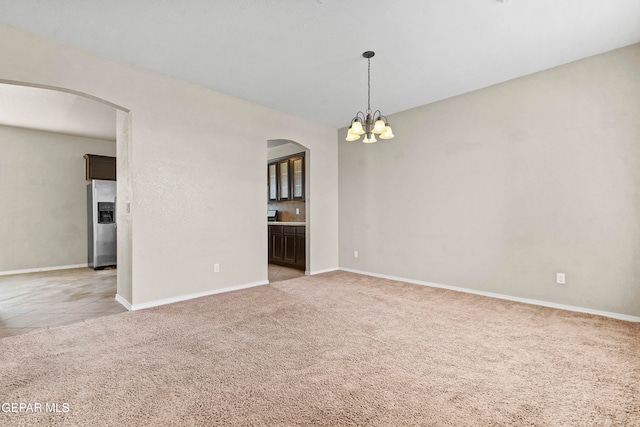 spare room featuring arched walkways, light carpet, and an inviting chandelier