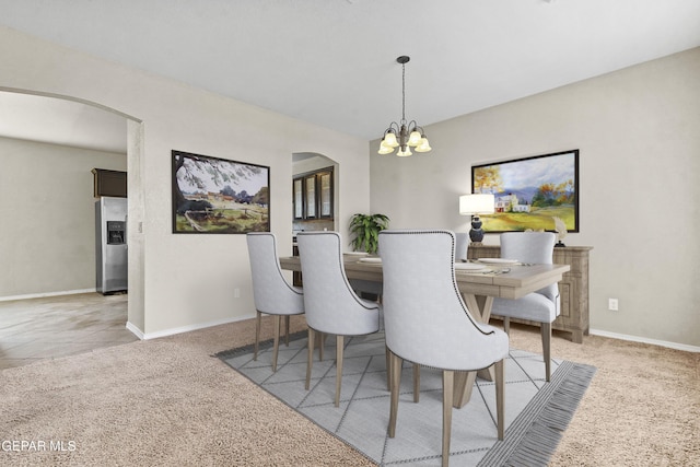 dining area featuring arched walkways, light carpet, a notable chandelier, and baseboards