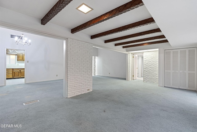 empty room with a notable chandelier, beam ceiling, light carpet, and brick wall