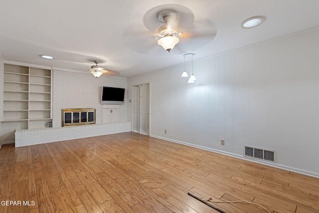 unfurnished living room with ceiling fan, a brick fireplace, built in features, wooden walls, and light wood-type flooring