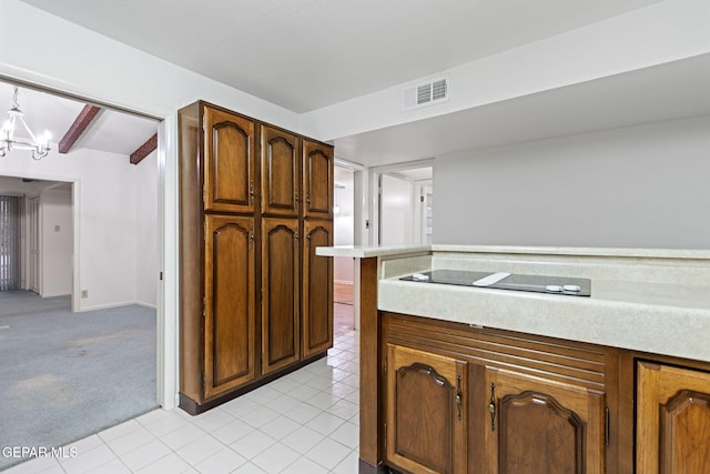 kitchen with black electric stovetop, a notable chandelier, and light colored carpet