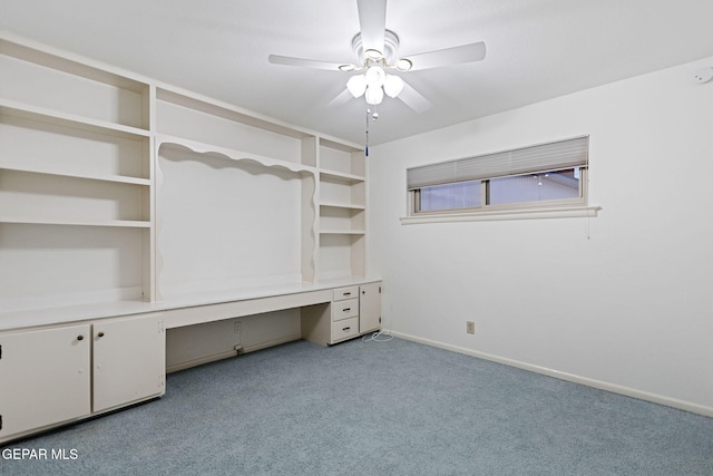 unfurnished office featuring built in desk, light colored carpet, and ceiling fan