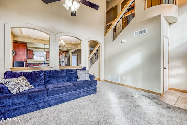 tiled living room featuring a high ceiling and ceiling fan with notable chandelier