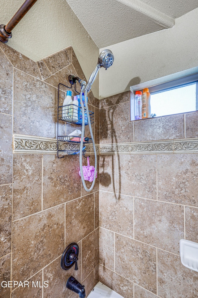 bathroom with a textured ceiling and tiled shower / bath