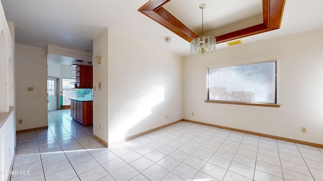 empty room featuring a notable chandelier, light tile patterned flooring, and a raised ceiling