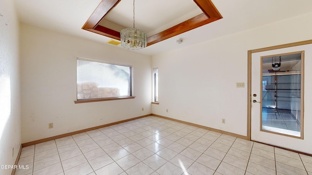 tiled empty room featuring an inviting chandelier and a raised ceiling