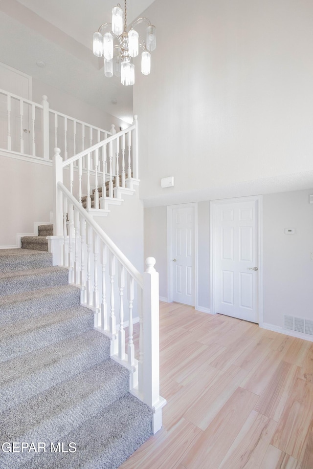 stairs featuring a notable chandelier, wood-type flooring, and a high ceiling