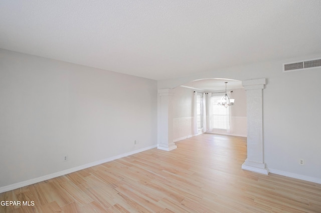 spare room with a chandelier, decorative columns, a textured ceiling, and light hardwood / wood-style flooring