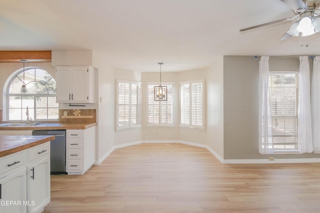 kitchen with wooden counters, sink, light hardwood / wood-style flooring, stainless steel dishwasher, and decorative light fixtures