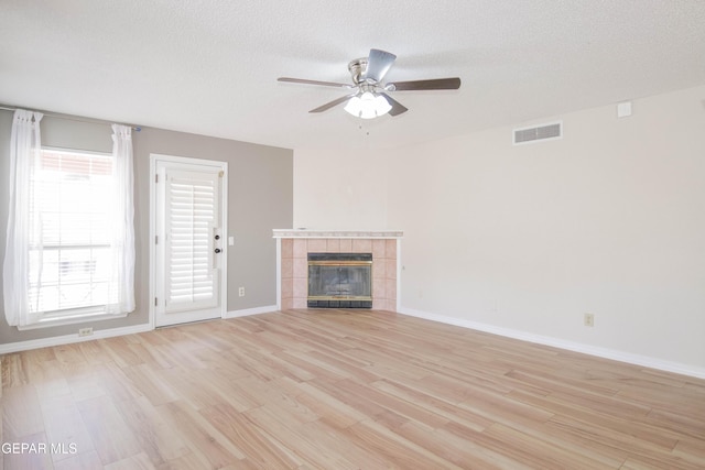 unfurnished living room with a textured ceiling, light hardwood / wood-style flooring, ceiling fan, and a tiled fireplace