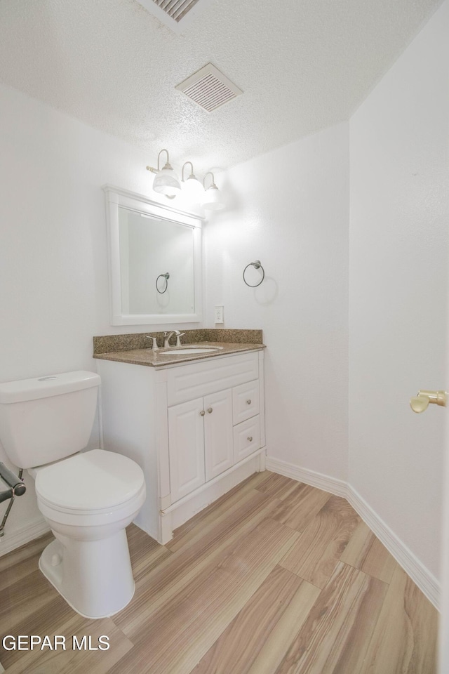 bathroom with a textured ceiling, vanity, hardwood / wood-style flooring, and toilet