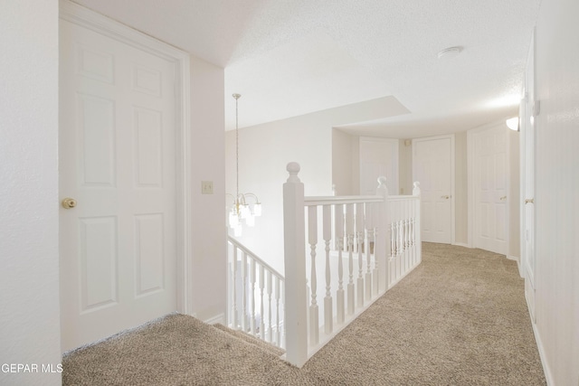 hall featuring light colored carpet, a textured ceiling, and an inviting chandelier