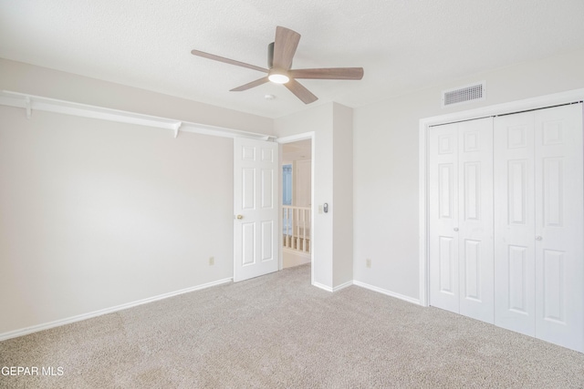 unfurnished bedroom with ceiling fan, a closet, light colored carpet, and a textured ceiling