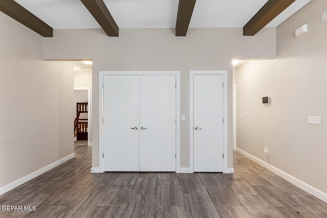 unfurnished bedroom featuring beam ceiling and dark wood-type flooring