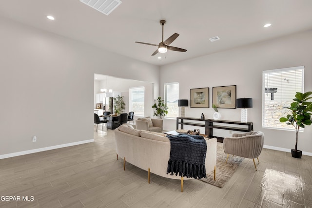 living room with ceiling fan with notable chandelier, a wealth of natural light, and light hardwood / wood-style flooring