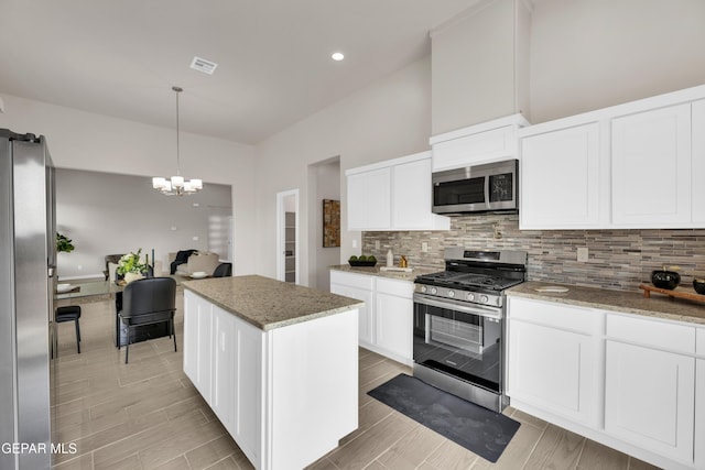 kitchen with a center island, white cabinets, appliances with stainless steel finishes, a notable chandelier, and light stone counters