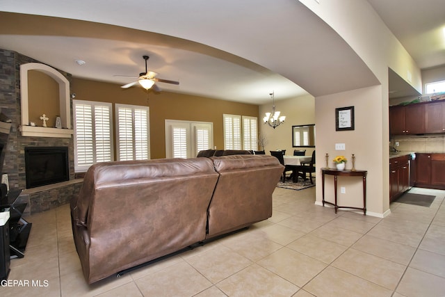 living room with light tile patterned floors, ceiling fan with notable chandelier, and a stone fireplace