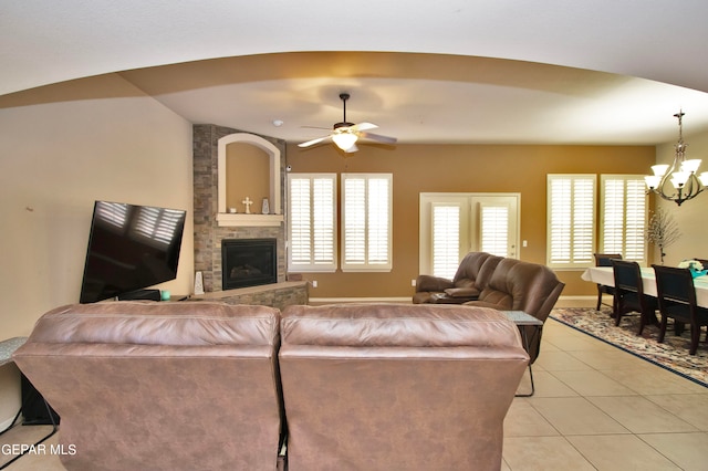 living room with ceiling fan with notable chandelier, light tile patterned floors, a fireplace, and vaulted ceiling