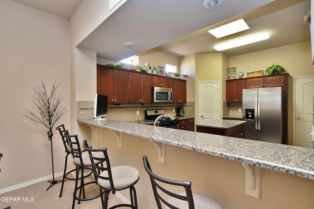 kitchen with tasteful backsplash, light stone countertops, a breakfast bar area, and appliances with stainless steel finishes