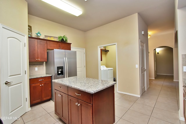 kitchen featuring a center island, light stone counters, stainless steel fridge, washer and clothes dryer, and light tile patterned floors