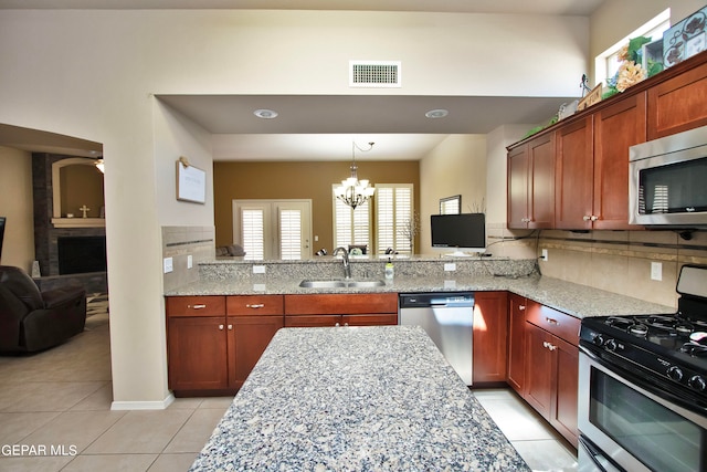 kitchen with light stone countertops, sink, stainless steel appliances, an inviting chandelier, and kitchen peninsula