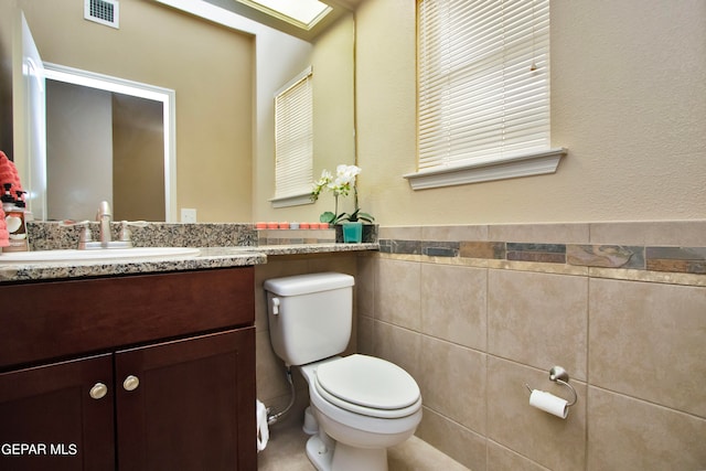 bathroom featuring vanity, toilet, and tile walls