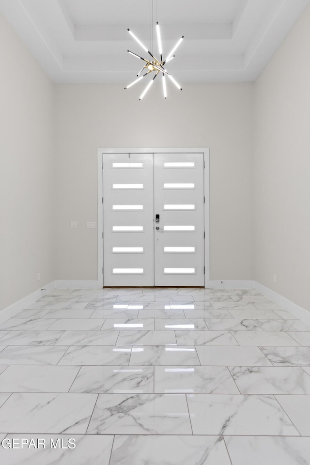 foyer with a raised ceiling and a chandelier