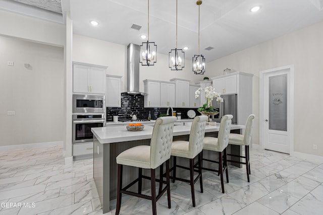 kitchen featuring decorative backsplash, appliances with stainless steel finishes, wall chimney range hood, hanging light fixtures, and an island with sink