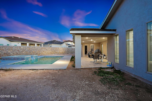 pool at dusk with an in ground hot tub and a patio