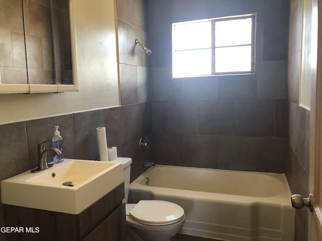 full bathroom with vanity, tiled shower / bath, tile walls, and toilet