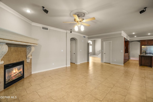 unfurnished living room with a tiled fireplace, ceiling fan, and ornamental molding